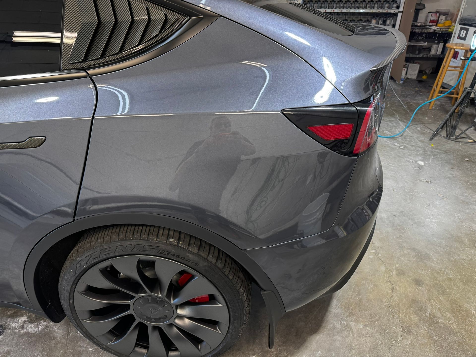 Gray Tesla Model Y with black rims and red brake calipers, parked indoors.