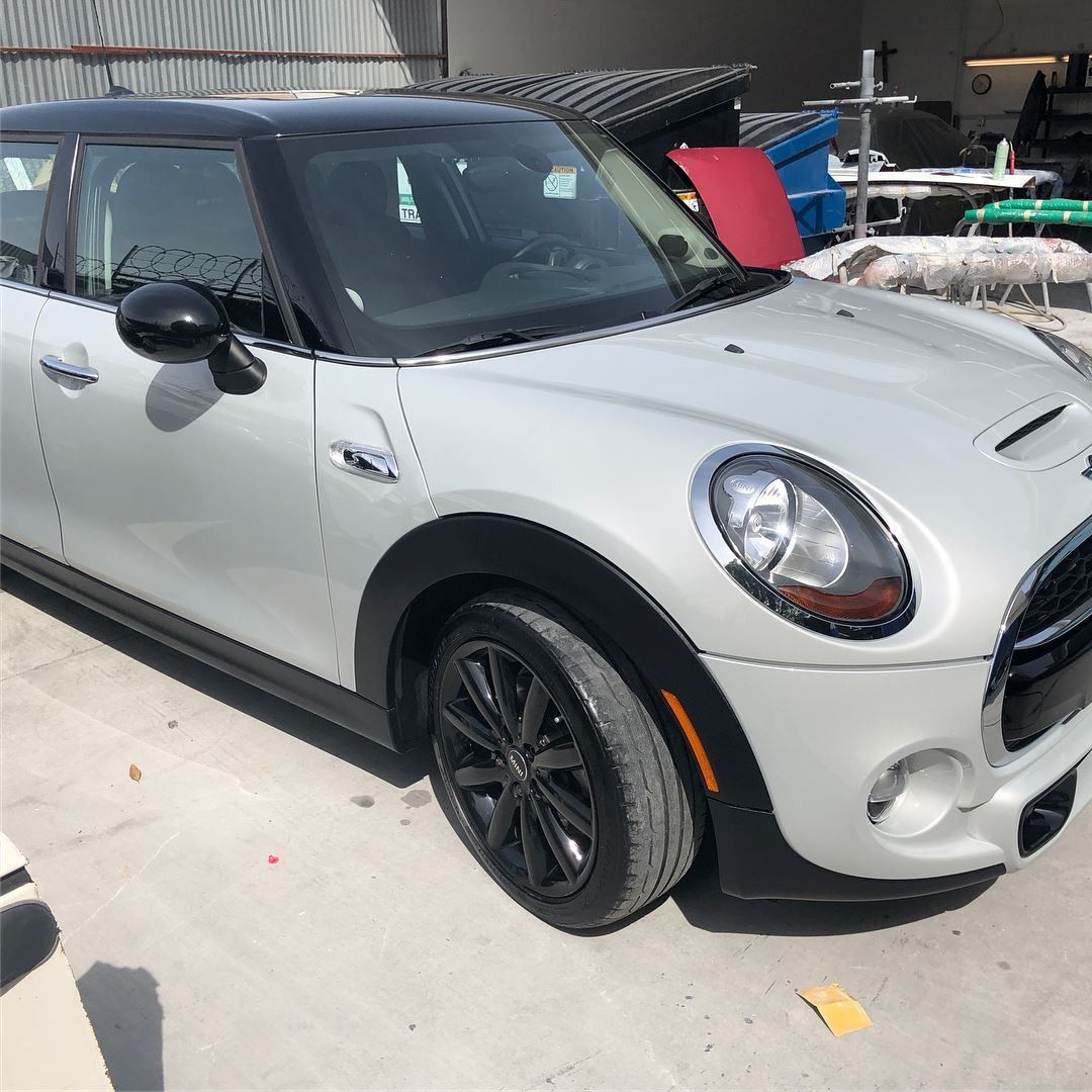 Silver MINI Cooper with black roof and wheels parked outside.