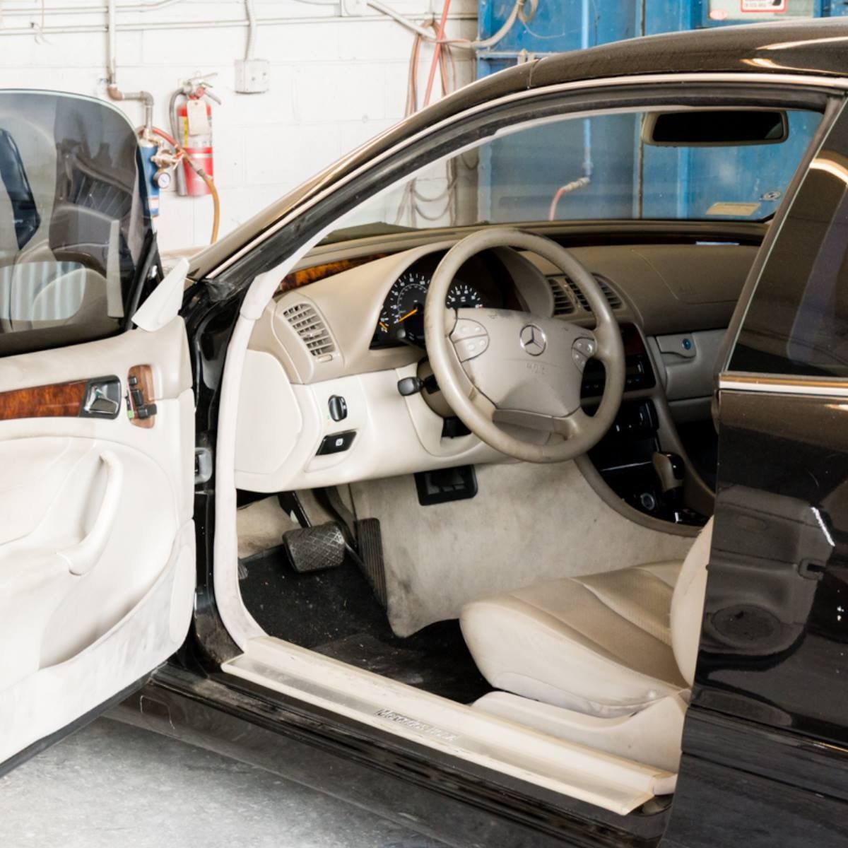 Interior of a black Mercedes coupe with the door open, showing a cream-colored interior and steering wheel.