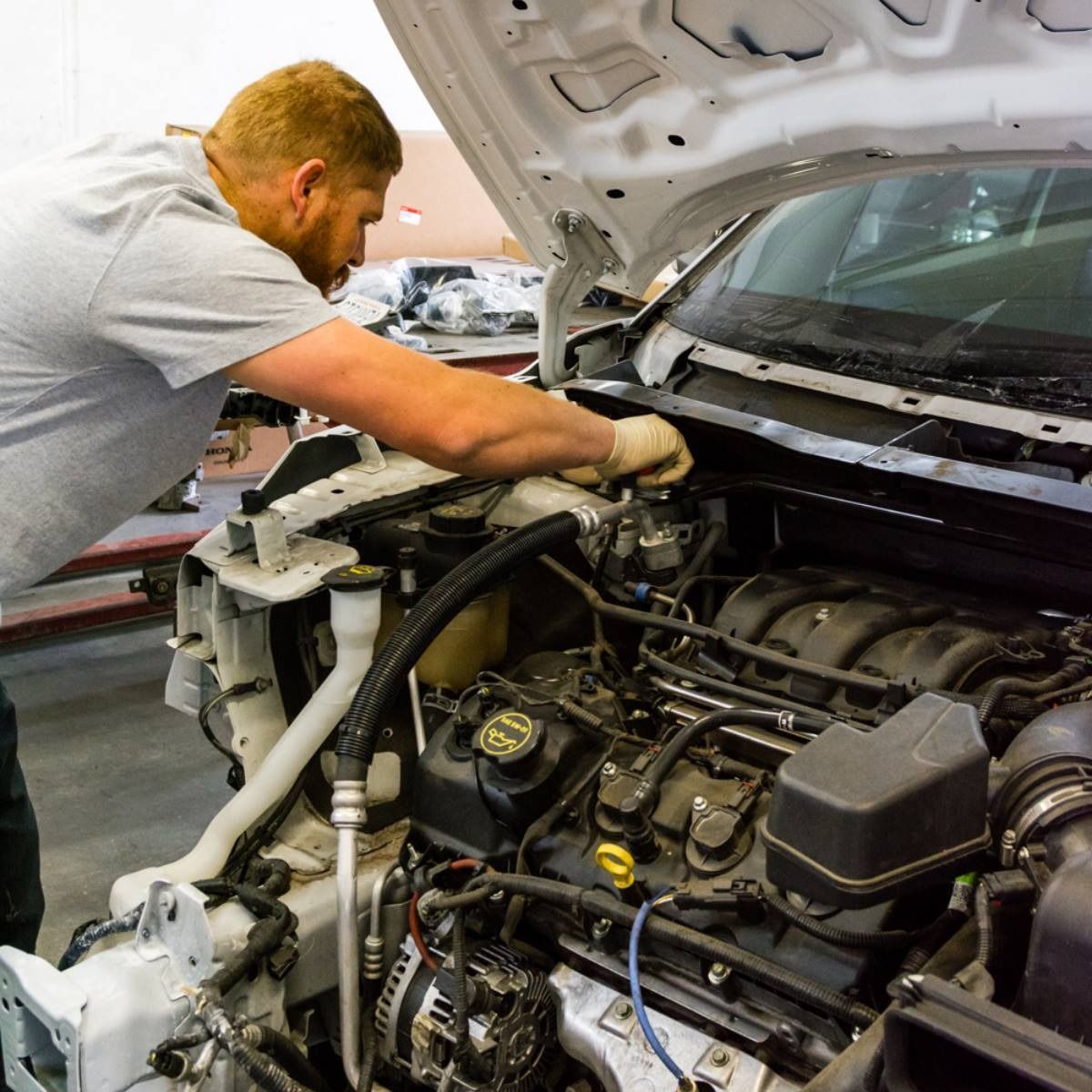 Mechanic working on the engine of a car with the hood open.