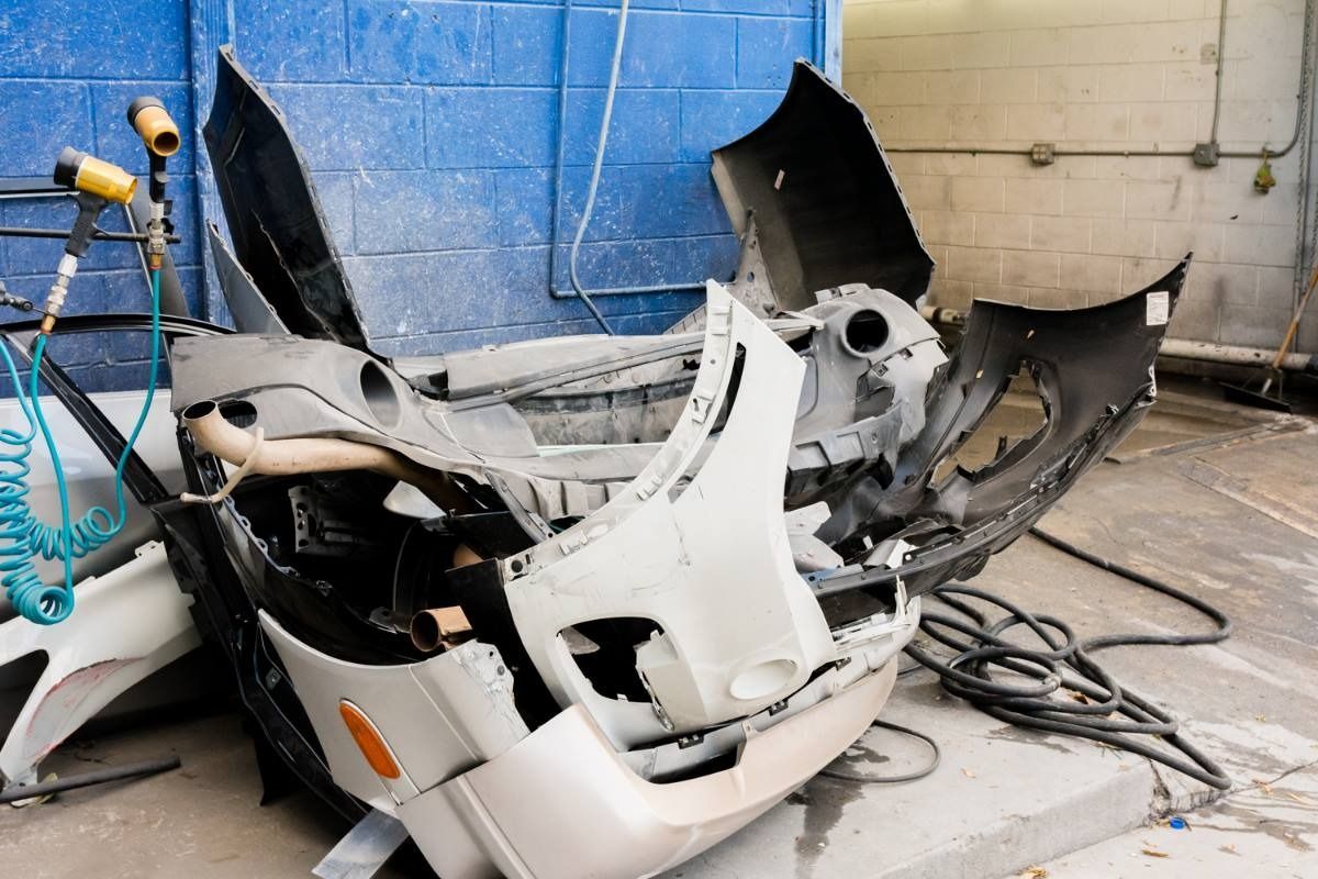 Damaged car bumper in a repair shop, white and black pieces, against a blue wall.