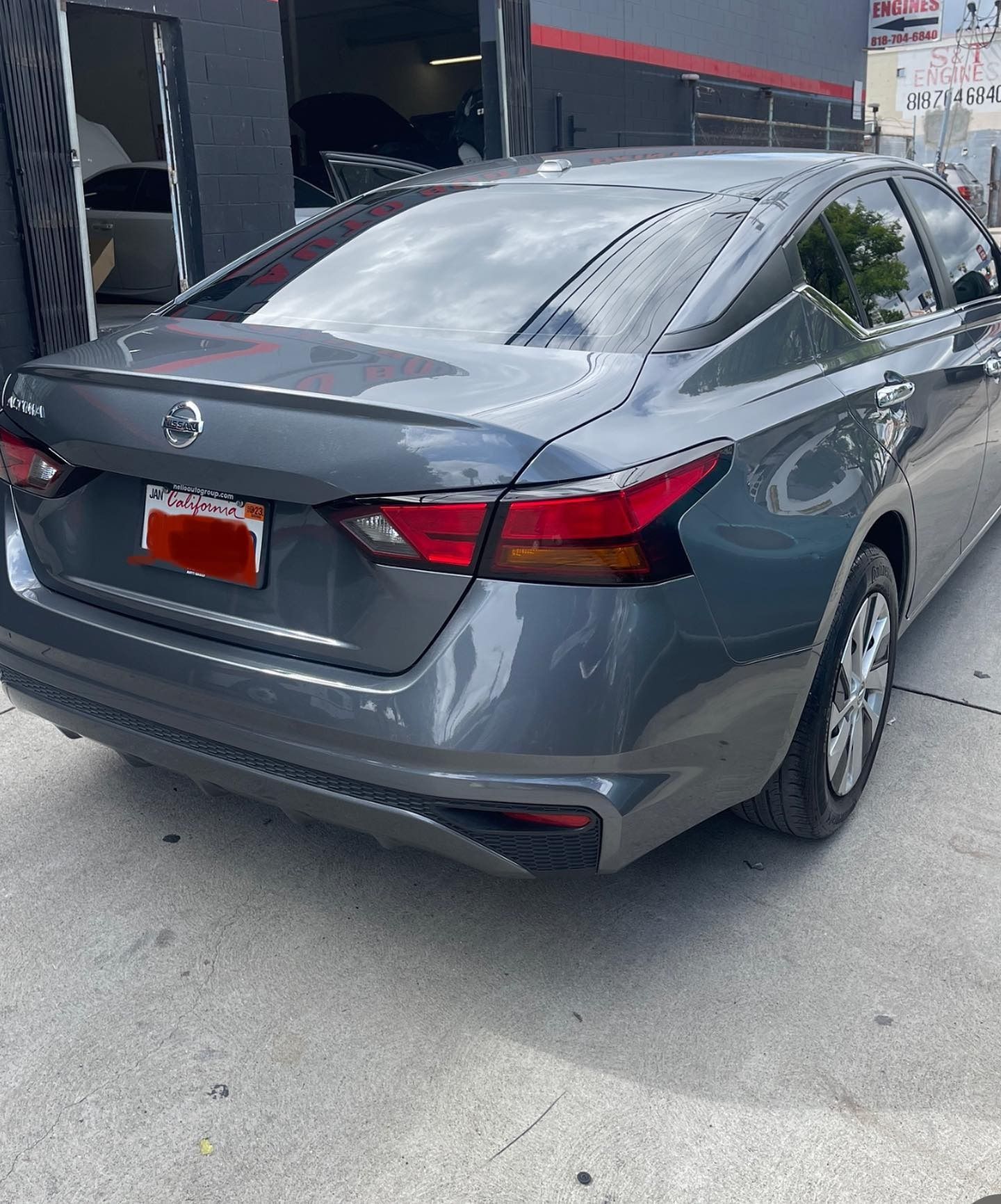 Gray Nissan Altima sedan parked in front of a building with a red license plate.