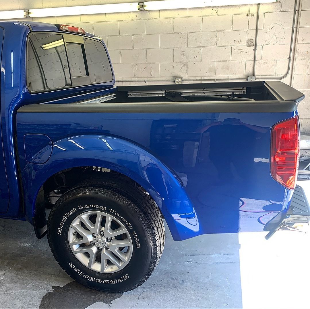 Blue pickup truck parked, detail of the rear tire, bed, and taillight.