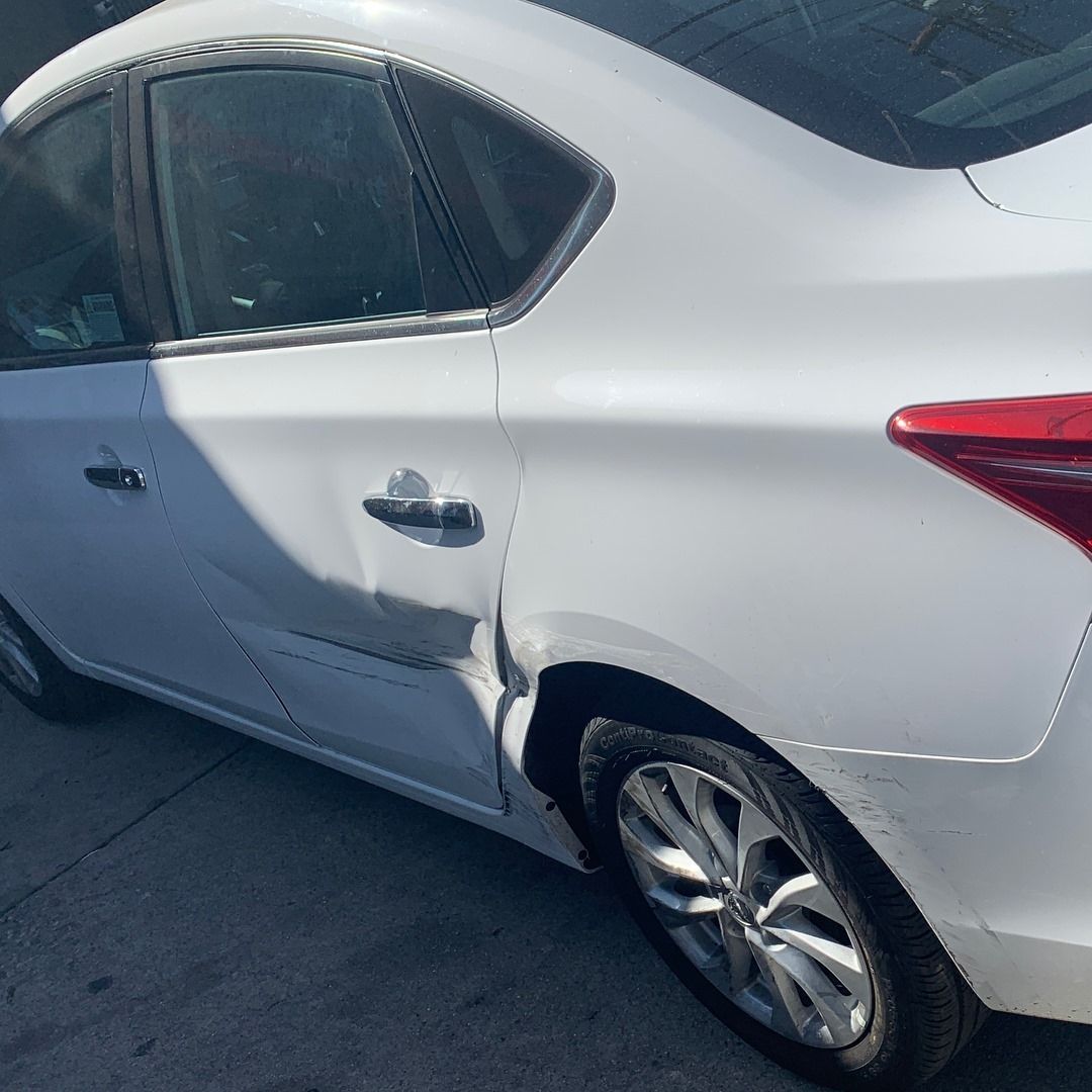 White sedan with significant damage to the driver's side rear door and quarter panel.