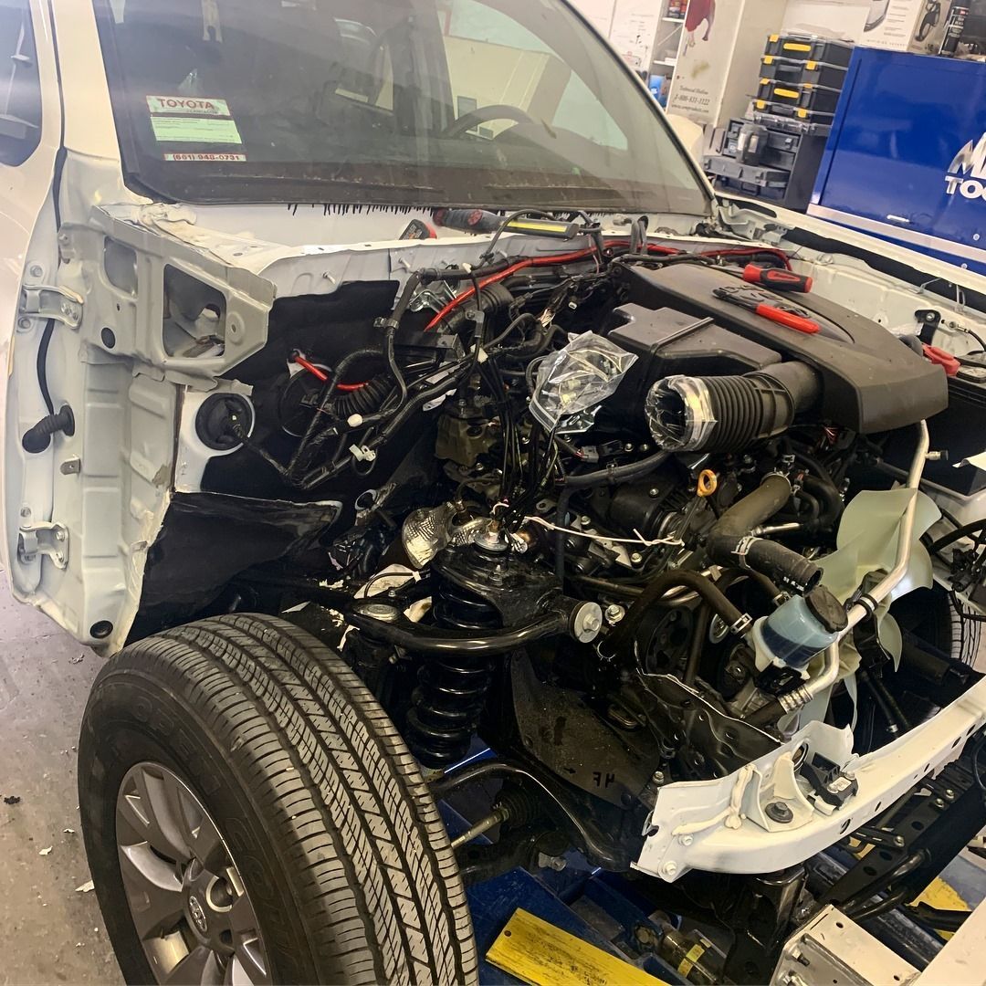 White car undergoing repair, engine exposed, in a workshop setting.