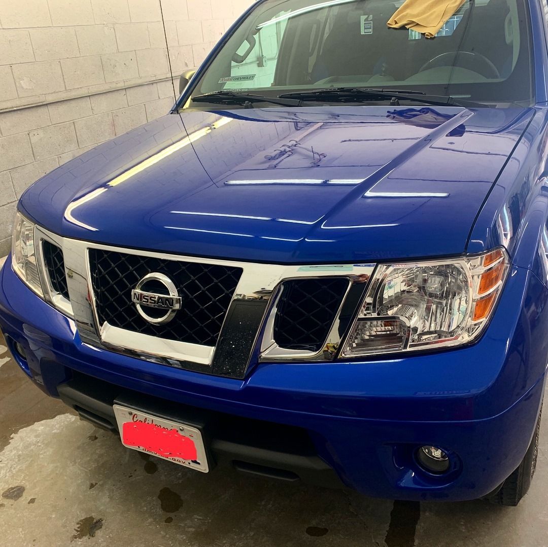 Blue Nissan Frontier truck with chrome grill and headlights, in a garage setting.