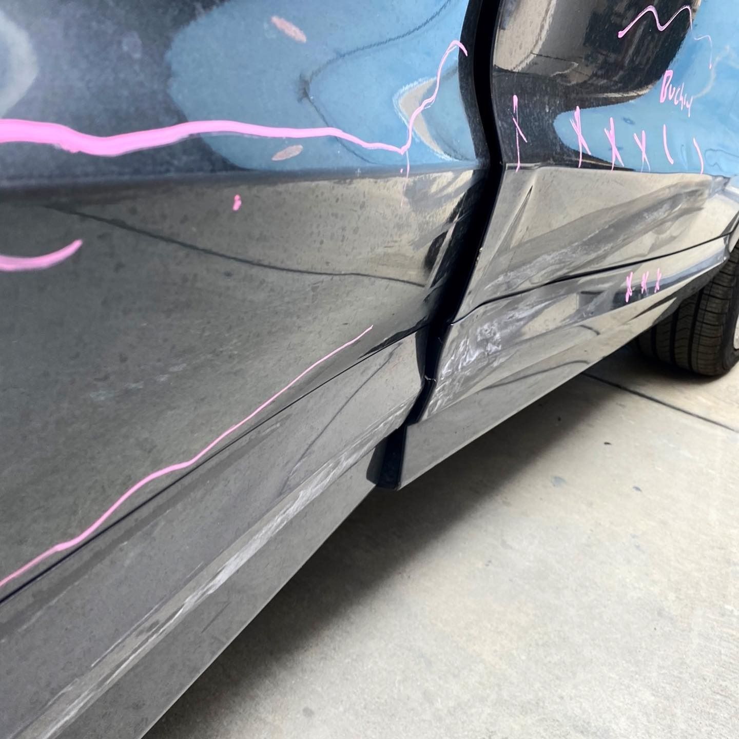 Damaged black car door with pink paint splatter, parked on concrete.