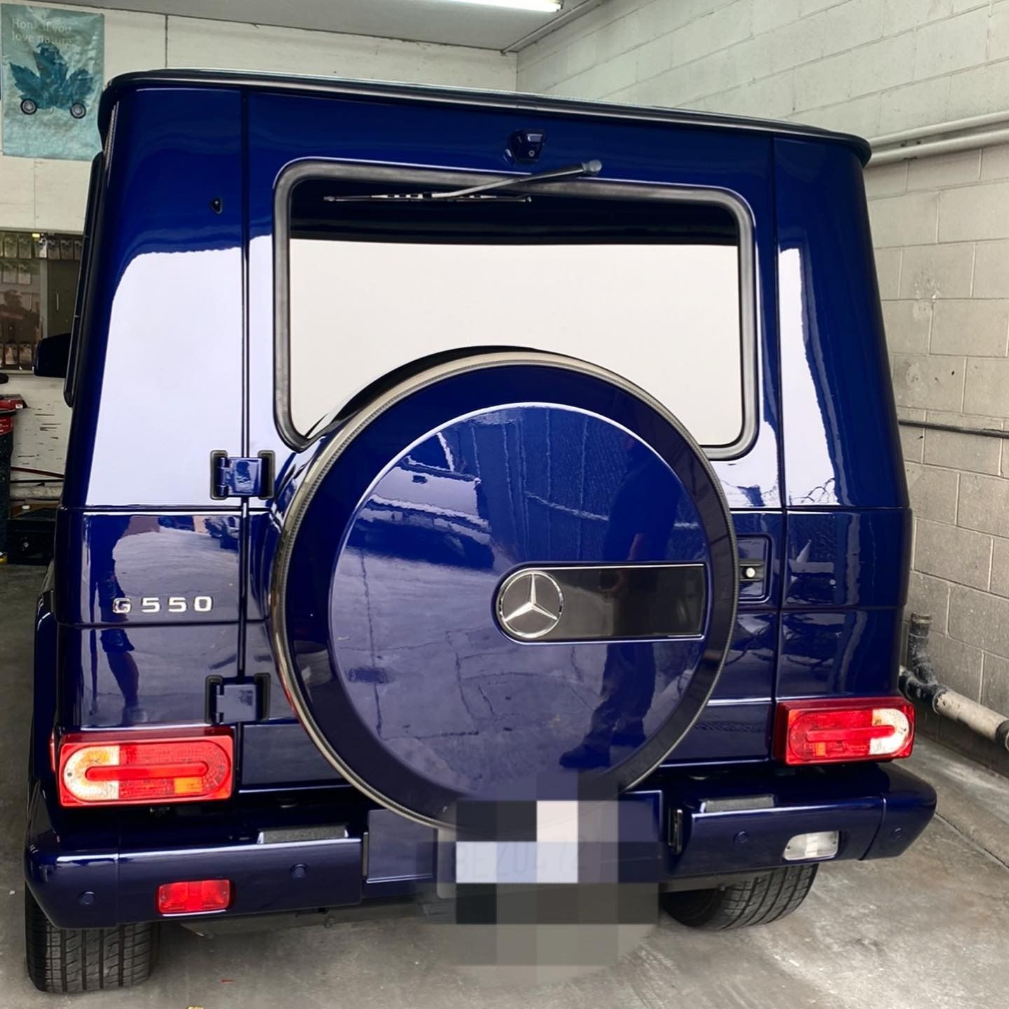 Blue Mercedes-Benz G550 SUV, rear view. Spare tire on back, red taillights, white trim, in a garage.
