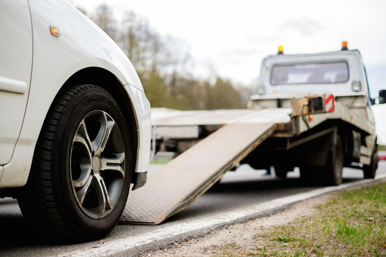White car being loaded onto a tow truck on a roadside, silver ramp extended.