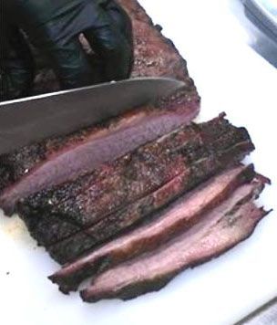 Black-gloved hand slicing smoked brisket on a white cutting board