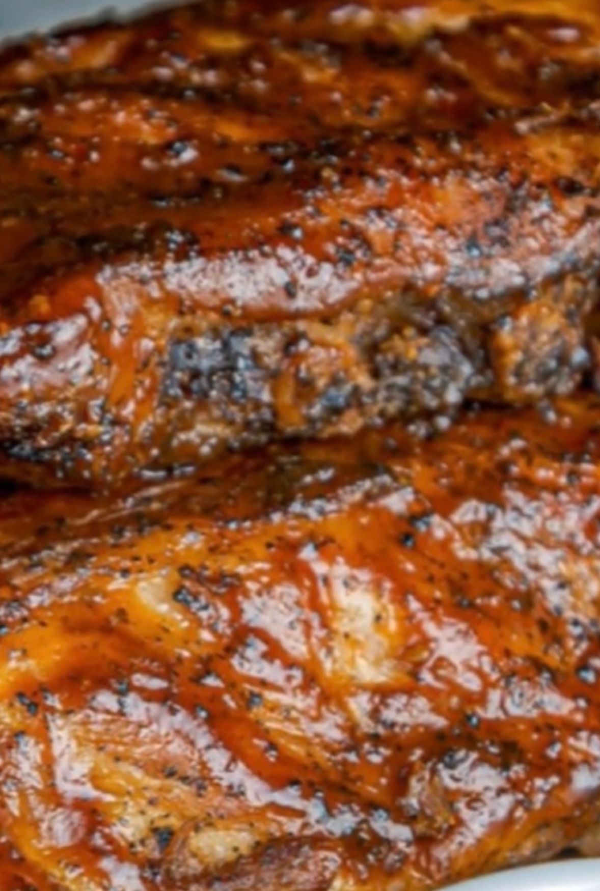 Close-up of BBQ ribs, glistening with sauce, showing char and meat