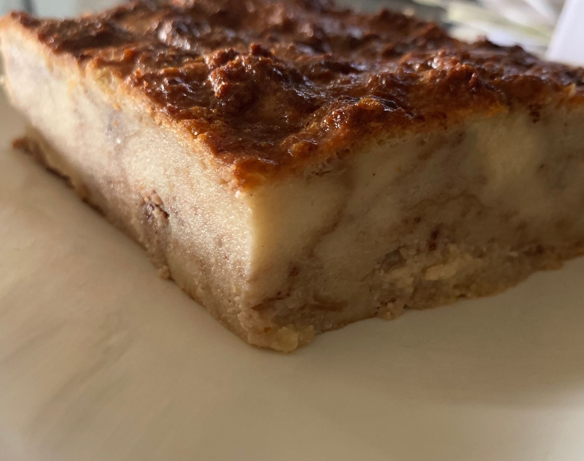 Bread pudding slice, golden crust, beige interior, on a white plate