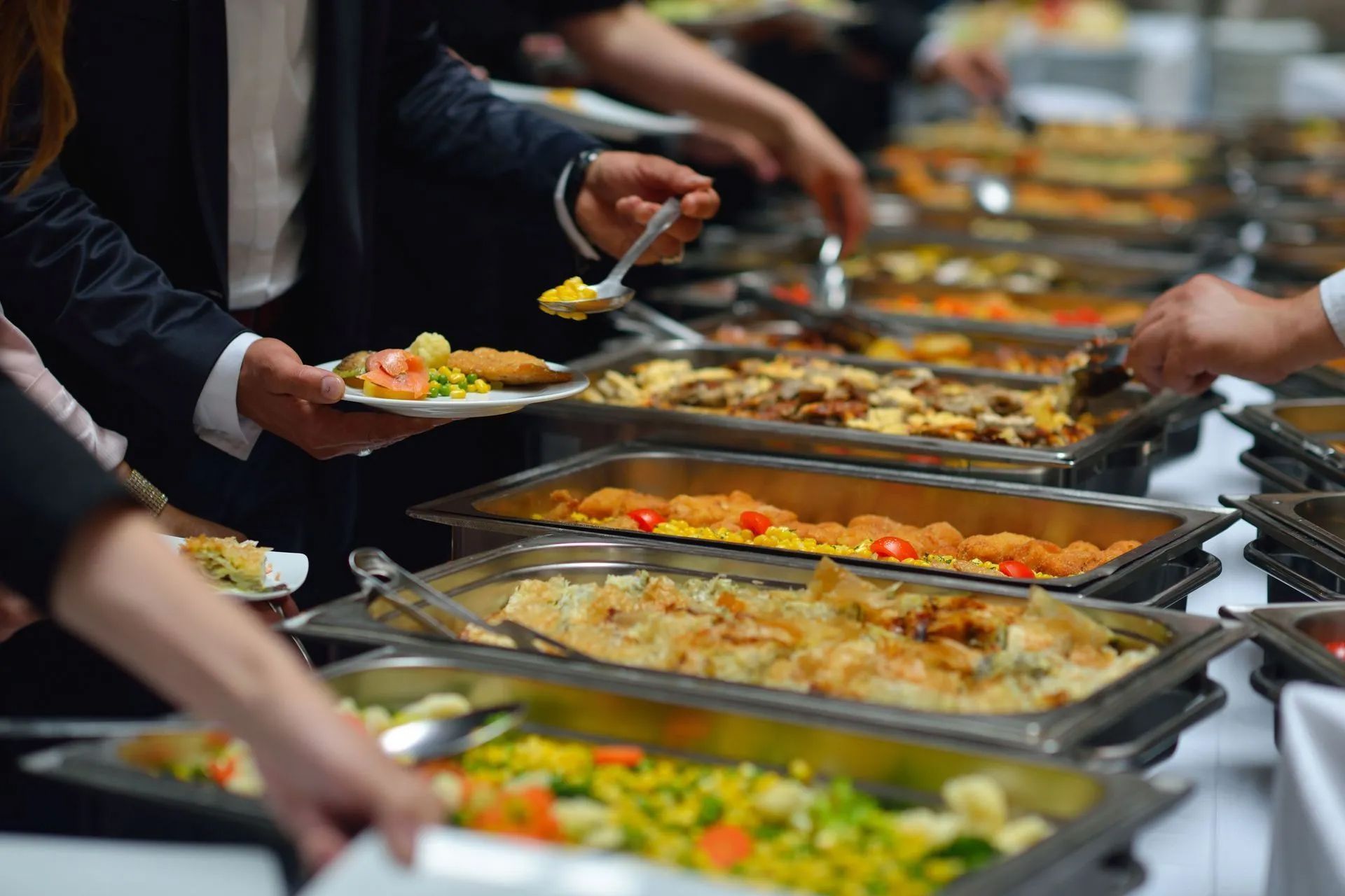 People at a buffet serving food onto plates. Various dishes in chafing dishes.