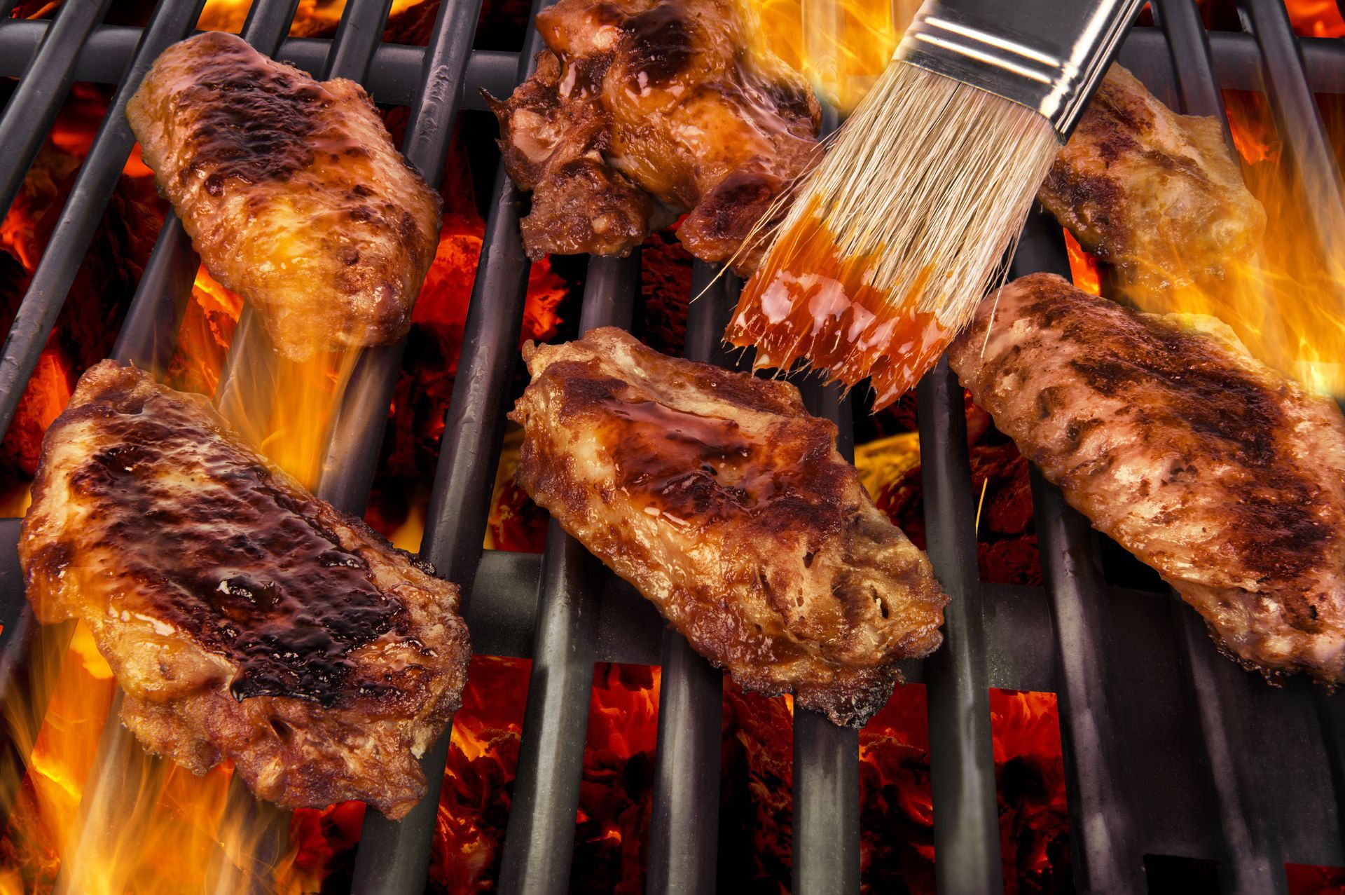 Chicken wings are being cooked on a grill with a brush