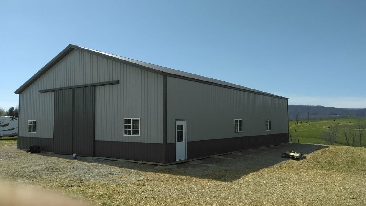 Gray metal barn-style building on a gravel lot under a clear blue sky