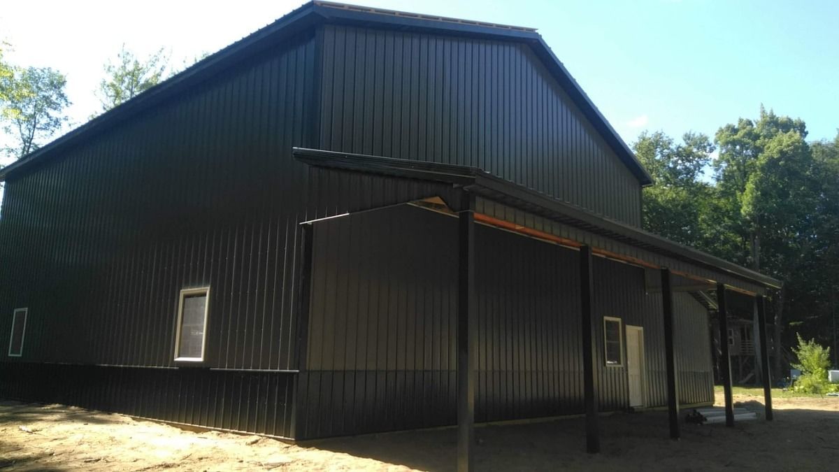 Black corrugated metal barn with a covered porch, set in a sunny wooded area