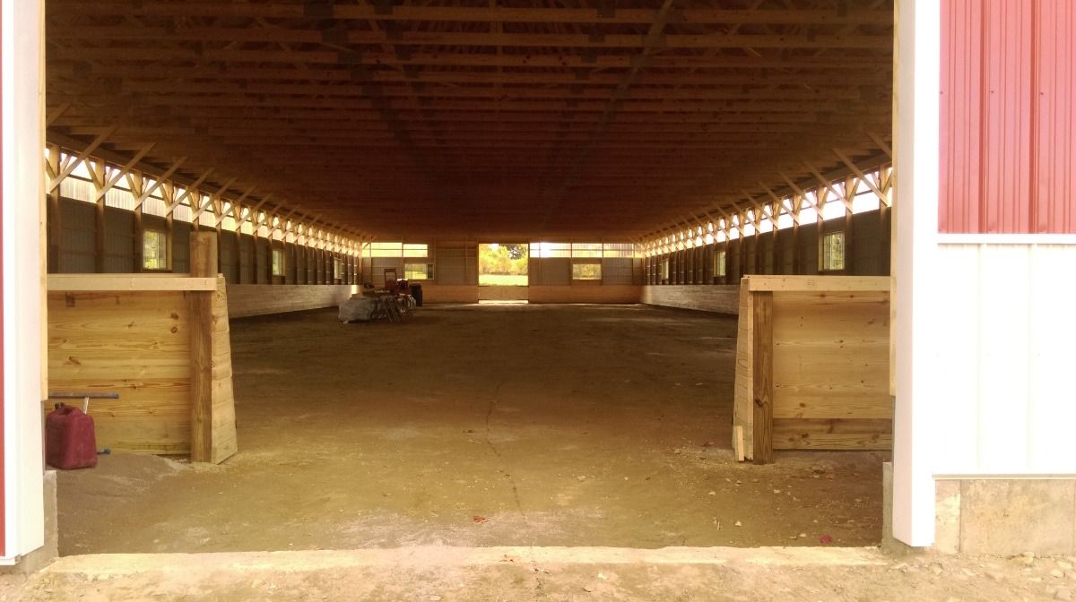 Open-sided barn interior with dirt floor and wooden stalls, lit by daylight at the far end