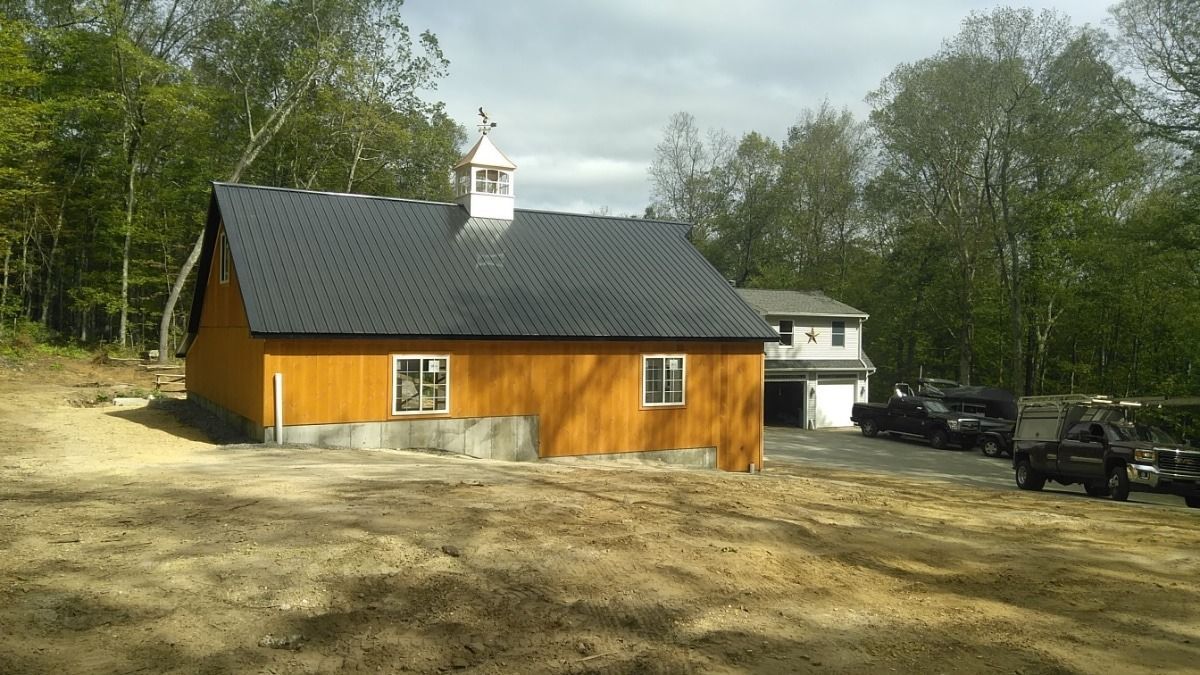 Orange building with dark roof in a wooded clearing, with parked vehicles nearby on a dirt lot
