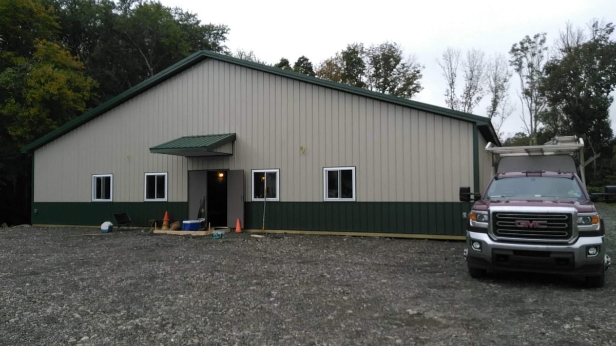 Large beige metal building with green trim and a truck parked outside on a gravel lot