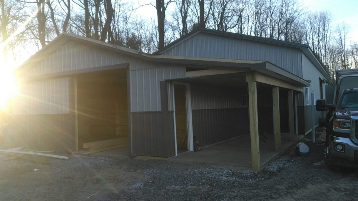 Metal barn with open bays and sun glare, set among bare trees beside a parked tractor.