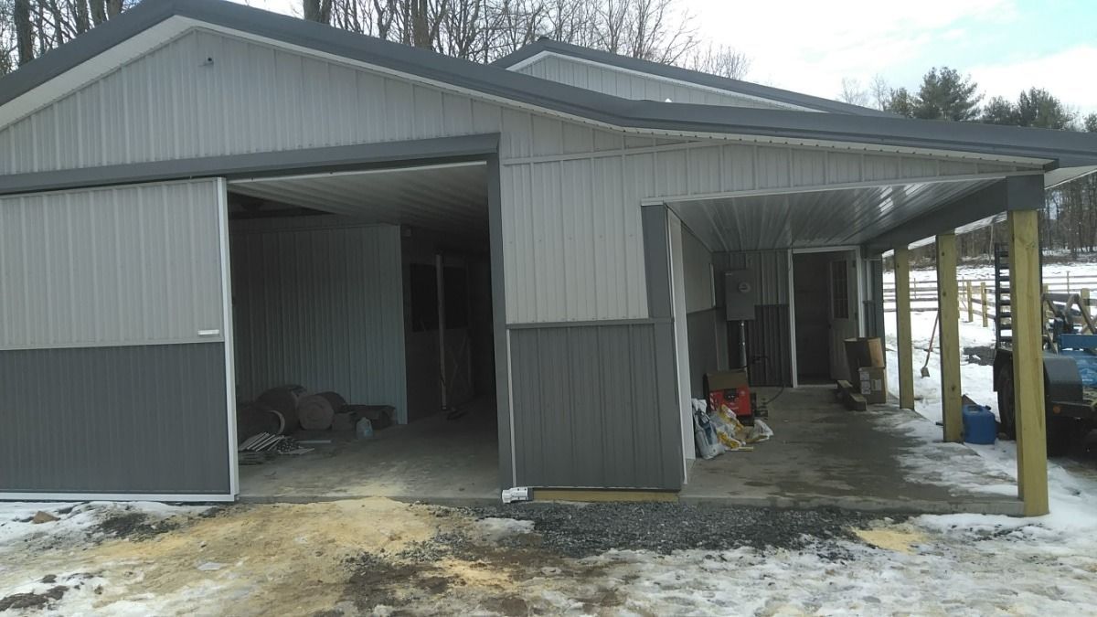 Snowy barn with two open bays and a covered porch, gray siding, and a blue post at the entrance