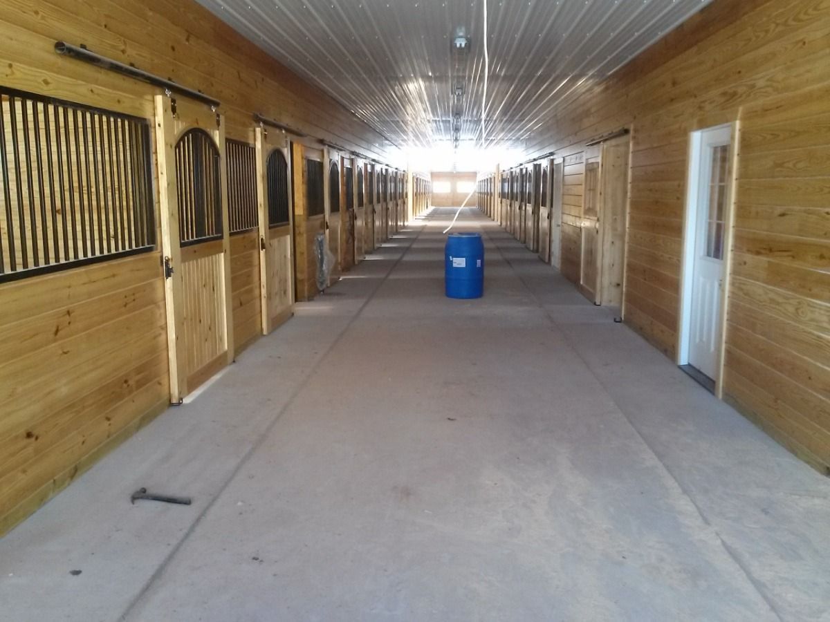 Empty wooden stable hallway with stalls on both sides and a blue barrel in the center.