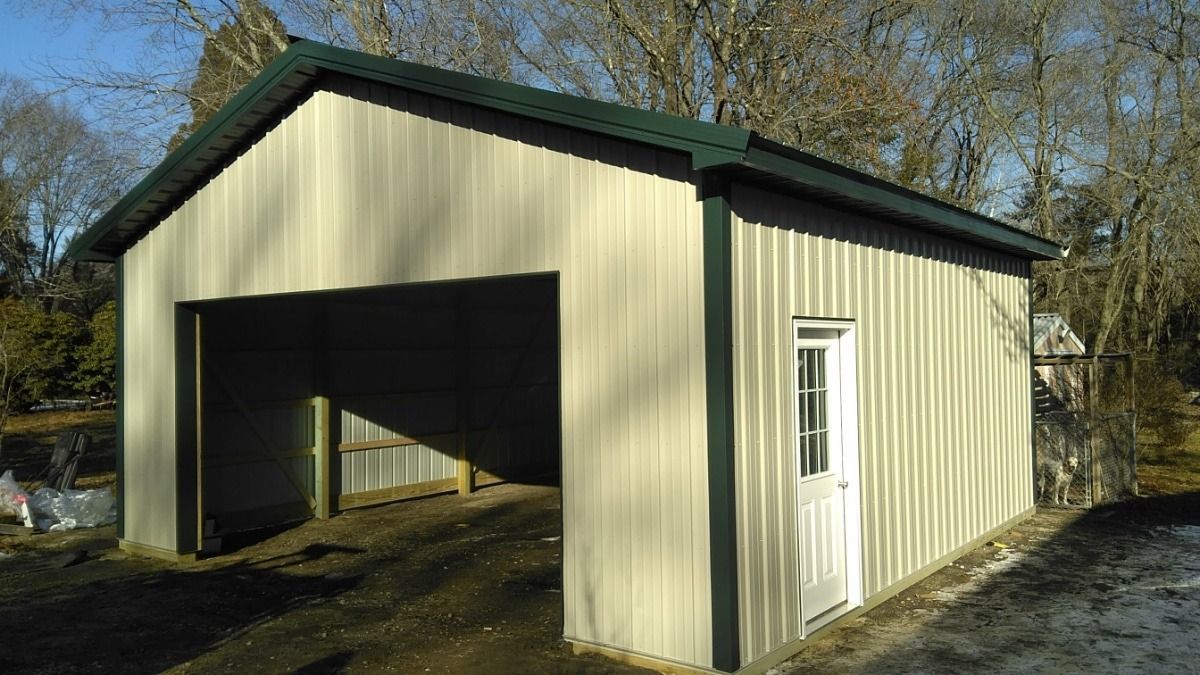 Beige metal shed with a large open bay door and a small side entrance, set among trees.