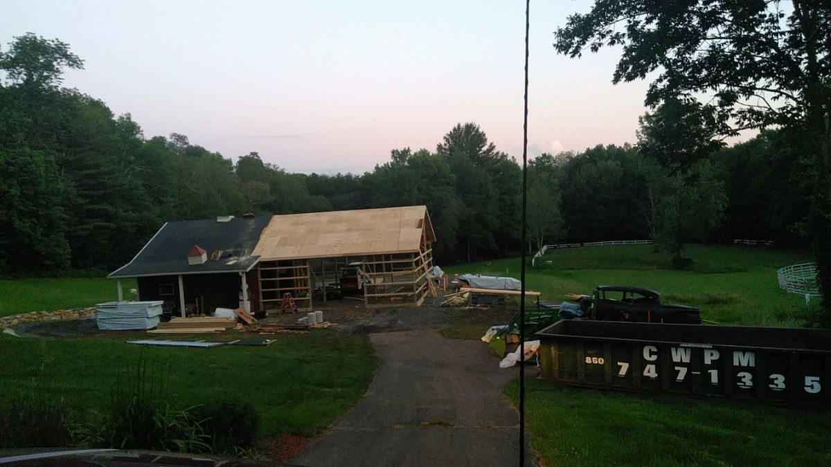 Rural yard with a partly damaged barn at dusk, surrounded by trees and a winding driveway.