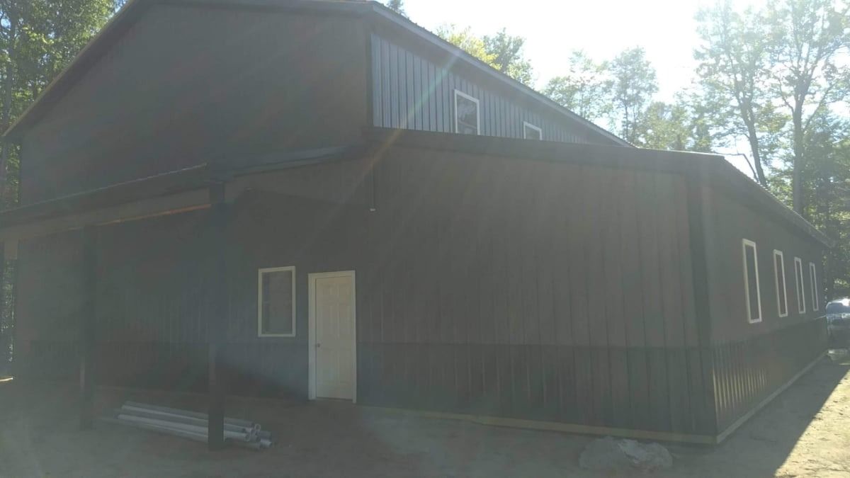 Dark barn-like building with a white door and windows in a sunny wooded area