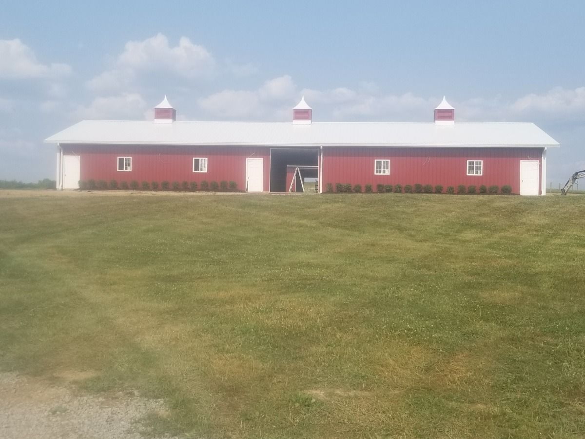 Red barn with white trim and cupolas on a grassy hill under a blue sky