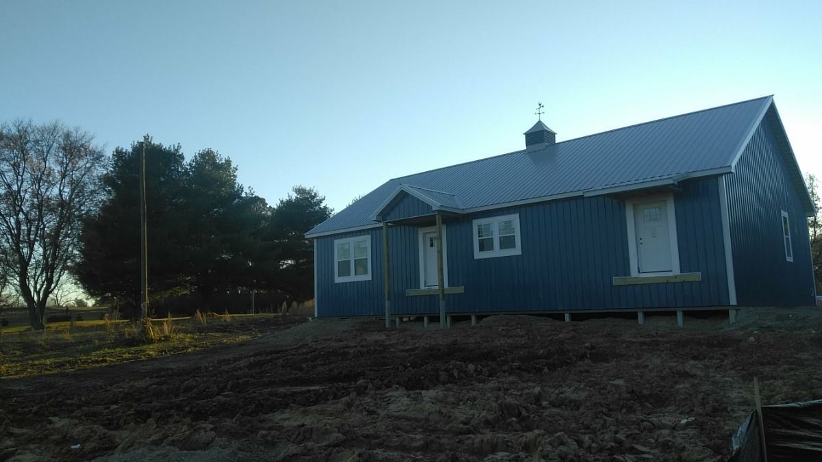 Blue house with a metal roof in a bare rural yard at dusk