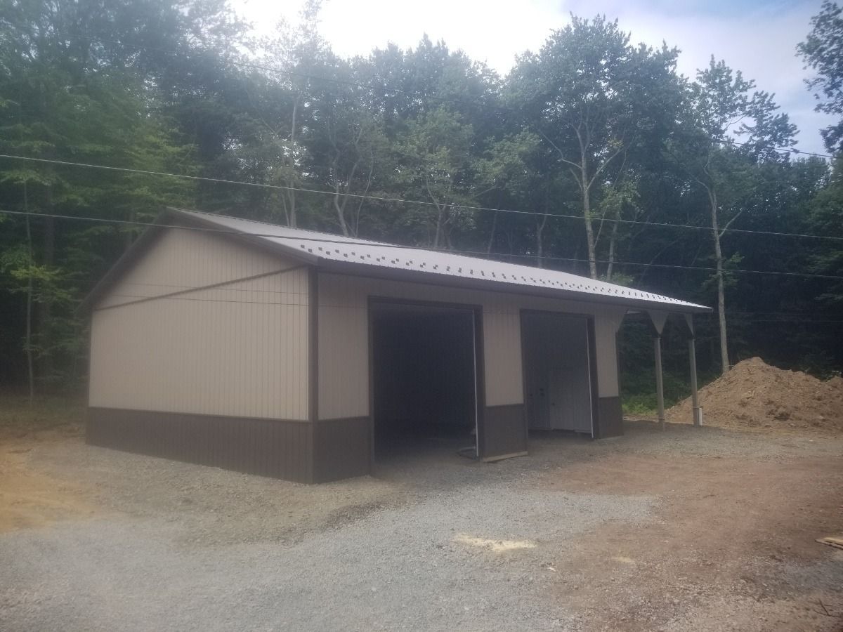 Small beige shed with open front in a gravel clearing beside a wooded area