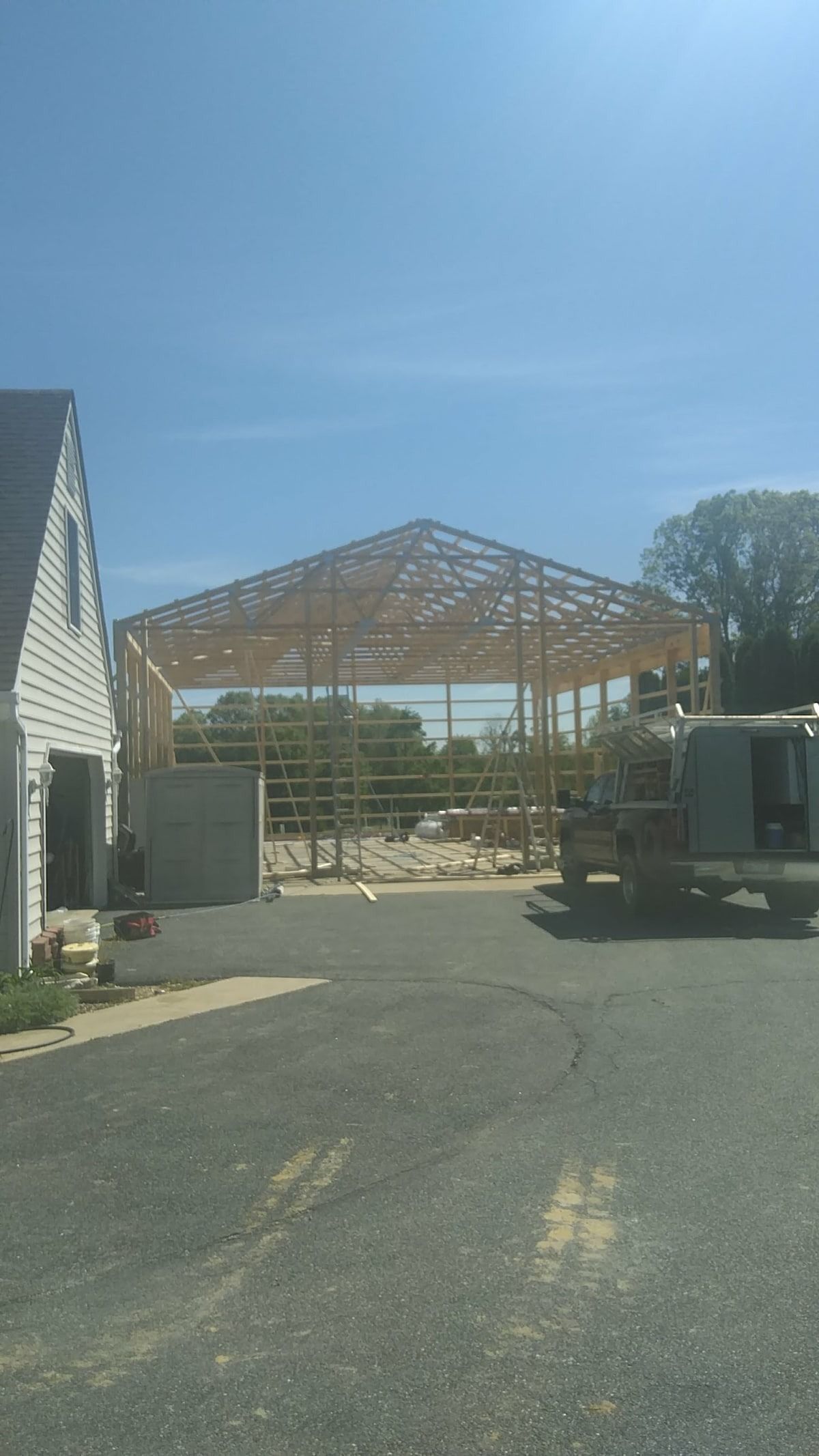 Partially built wooden structure in a paved yard beside a white building under a clear blue sky