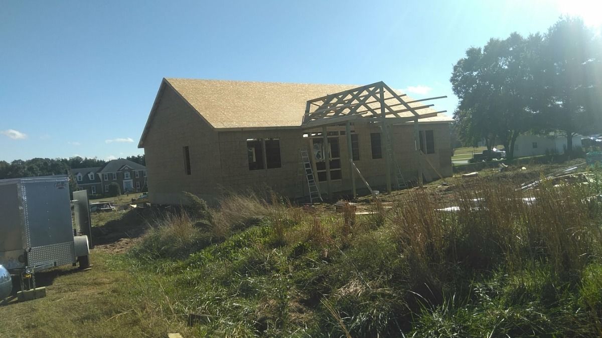 Partially built house with exposed roof framing in a sunny grassy field