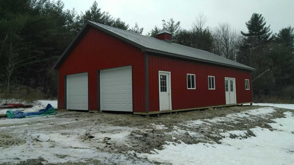 Red barn-style garage with two white doors in a snowy wooded area.