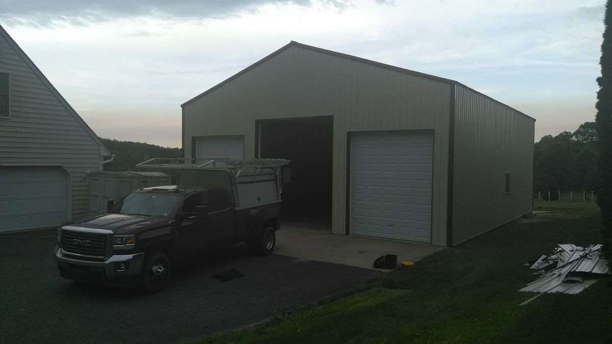White garage/workshop with open bay and roll-up door, black pickup parked outside at dusk.