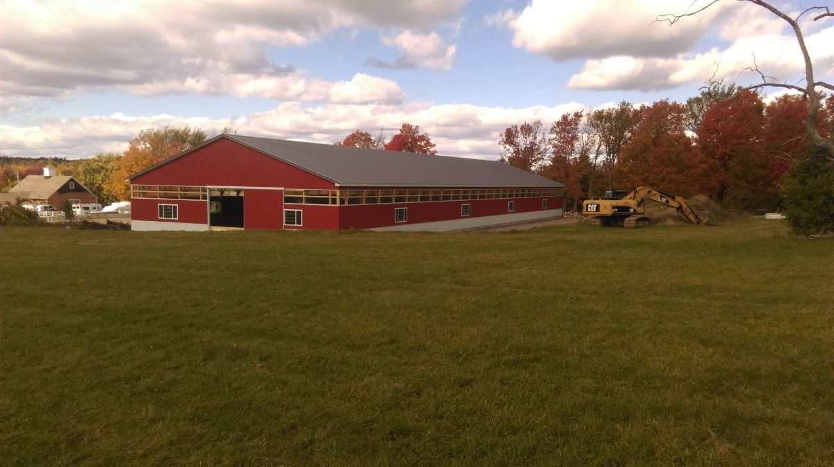 Red barn with long white trim on a grassy field under a cloudy autumn sky.