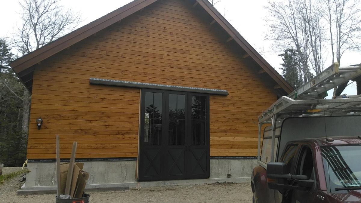 Wooden building with dark-framed glass doors, a van parked beside it, and bare trees in the background.