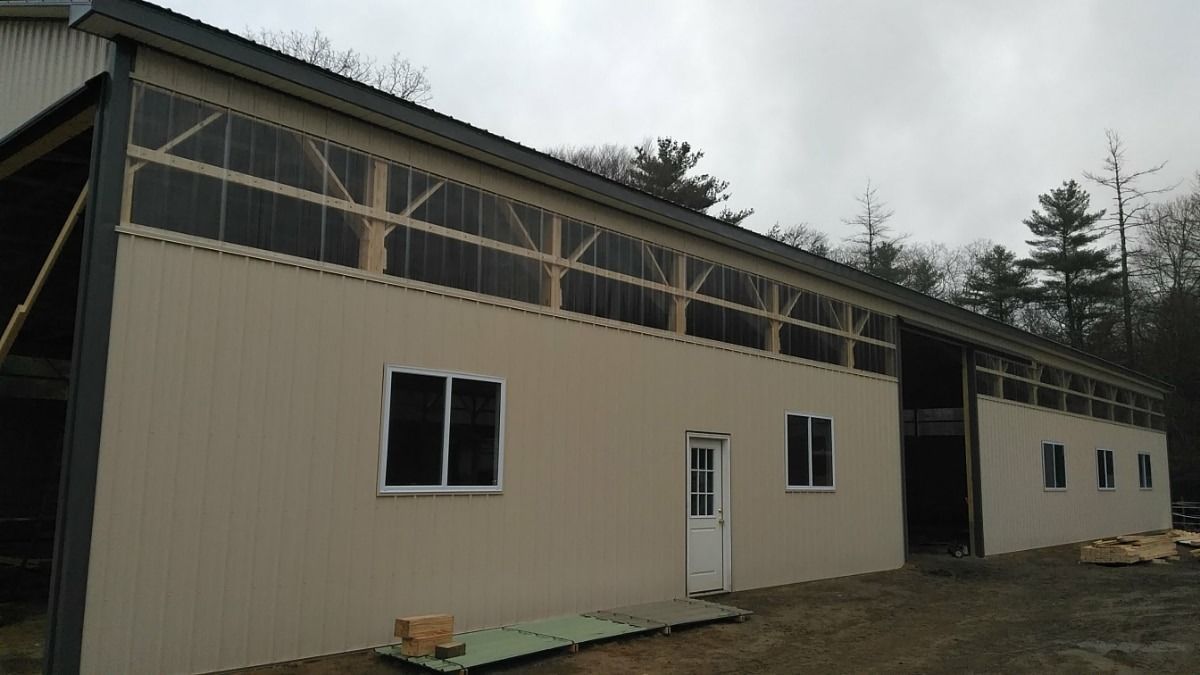 Unfinished beige metal building with white doors and windows in a wooded area