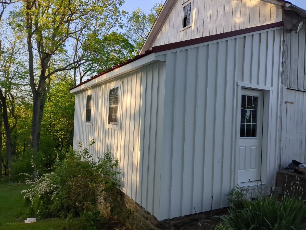 White wooden shed with a sloped roof beside trees in a sunny yard