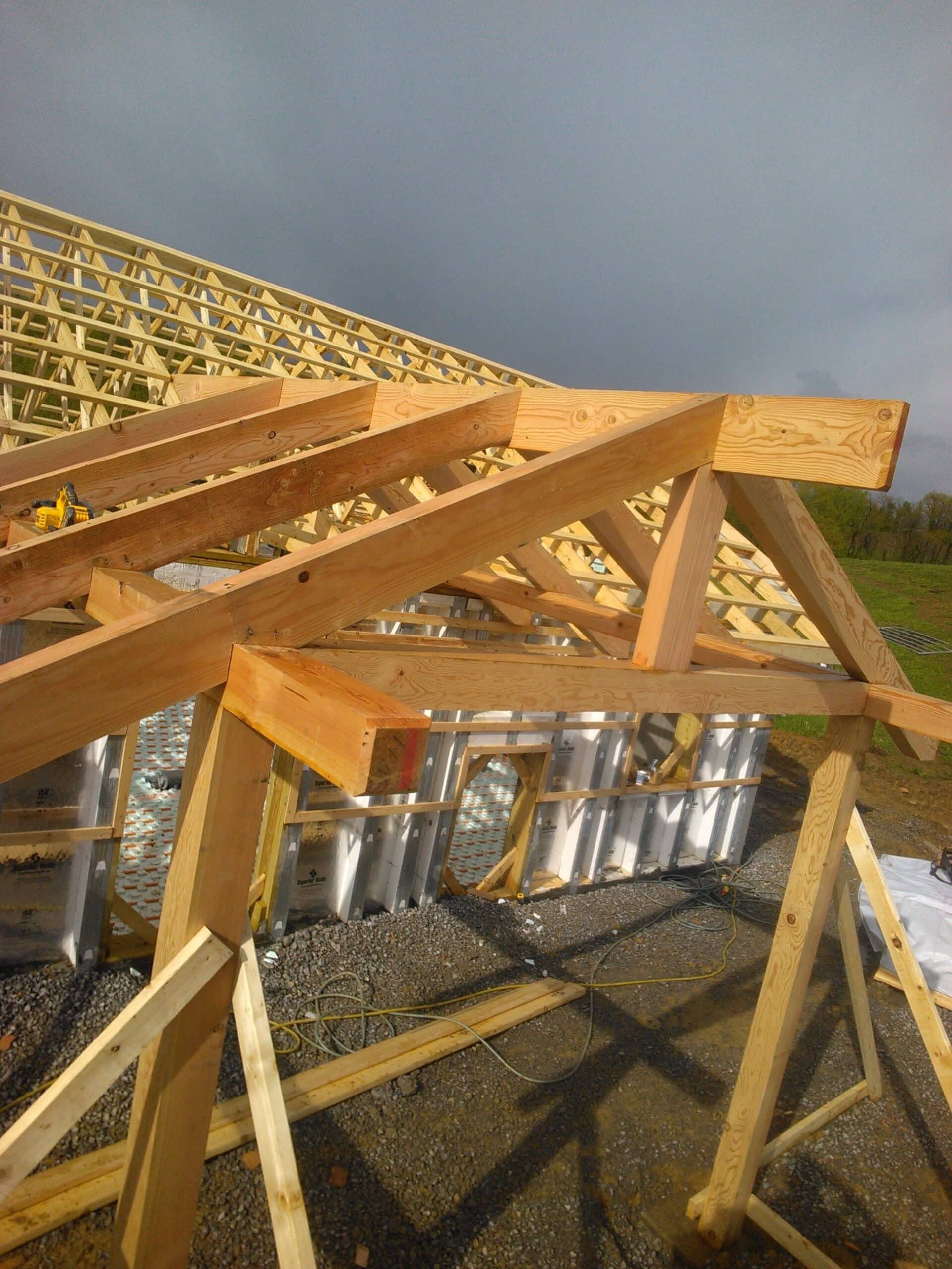 Wooden roof trusses under construction above a row of solar panels on a sloped roof