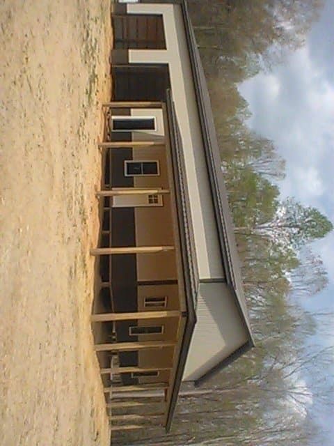 Single-story tan house with a covered porch on a sandy lot, surrounded by leafless trees.