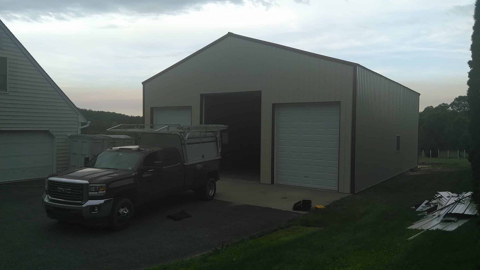Black pickup truck parked beside a large beige garage or workshop at dusk.
