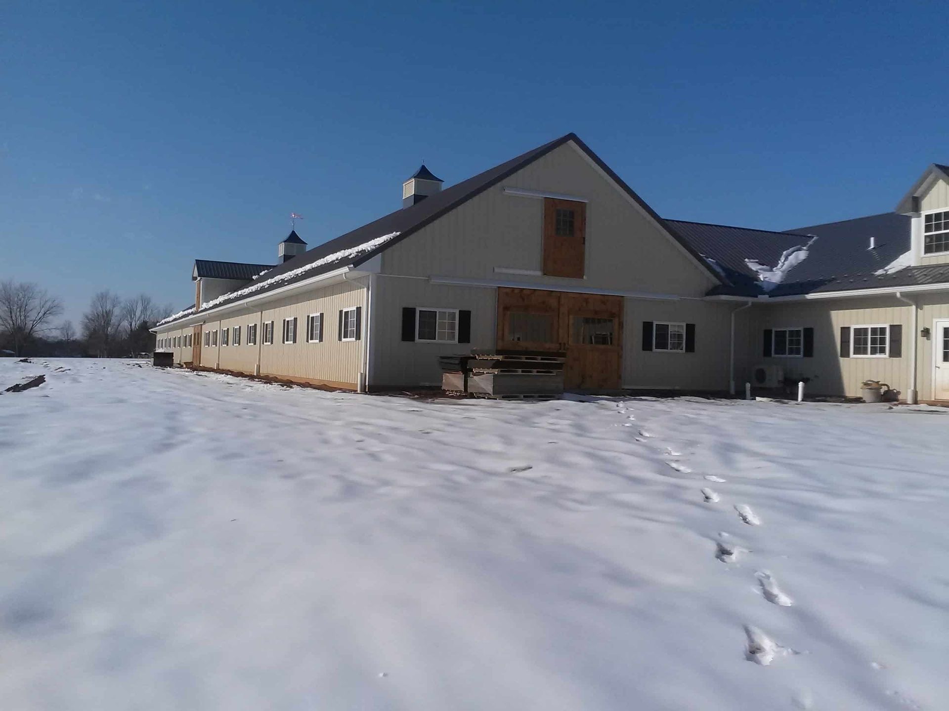 Snow-covered farmhouse under a clear blue sky with footprints leading to the front door