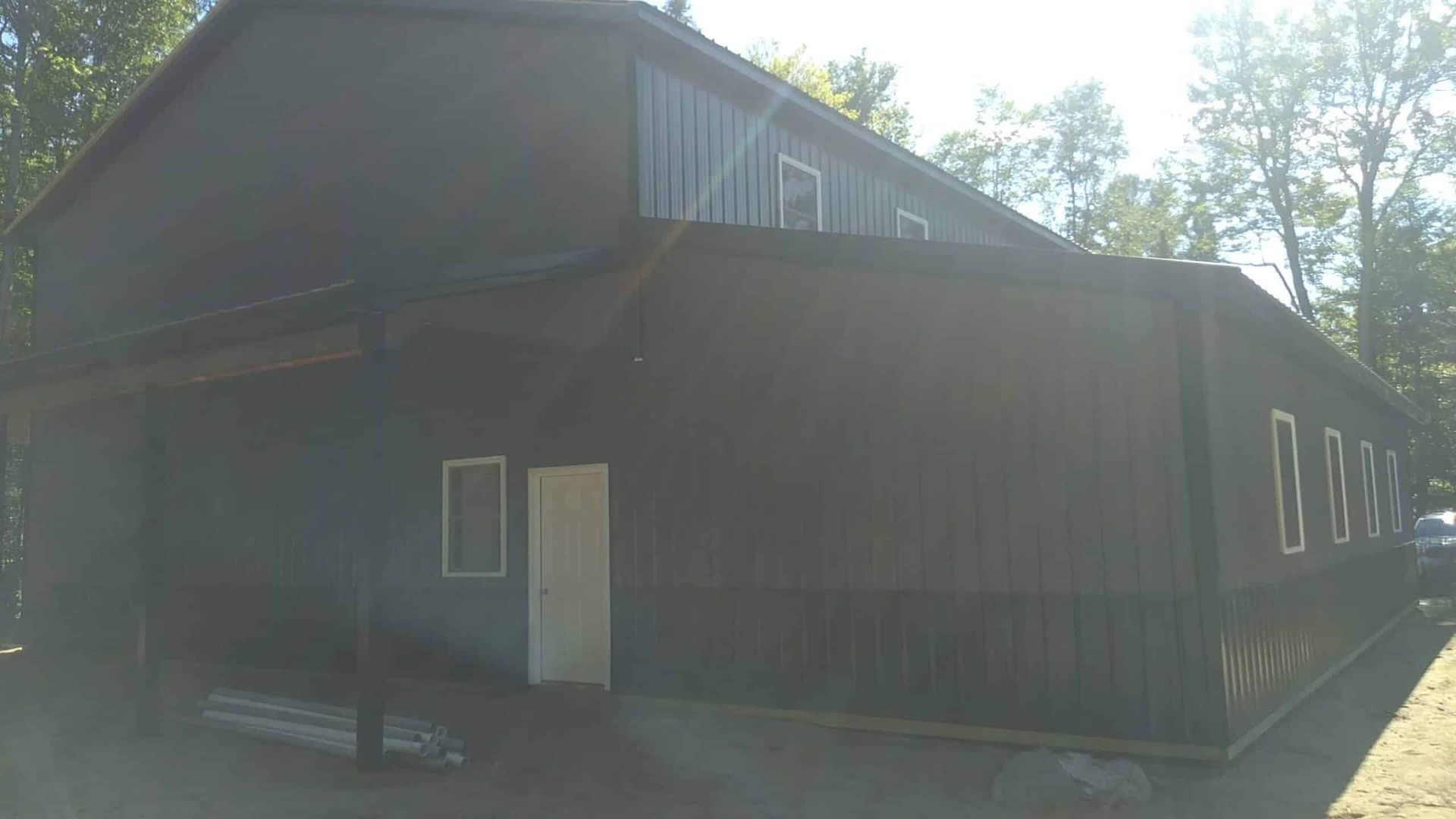 Dark wooden cabin exterior with a white door and windows, lit by bright sunlight and surrounded by trees