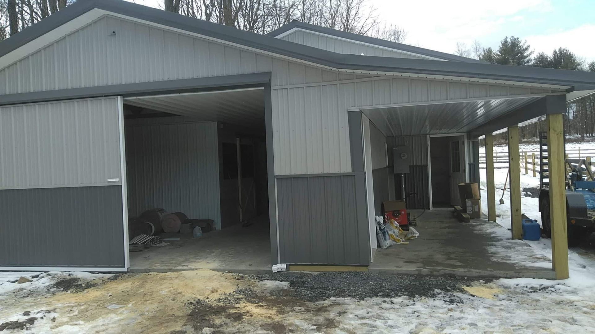 Metal-sided garage with open bays, snow on the ground, and a carport on the right