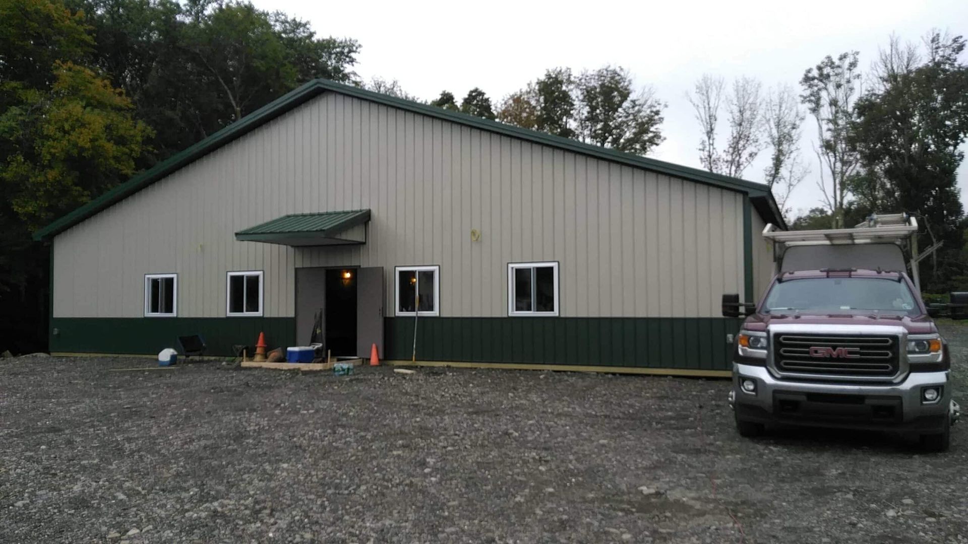Large beige metal building with green trim and a parked pickup truck on a gravel lot.