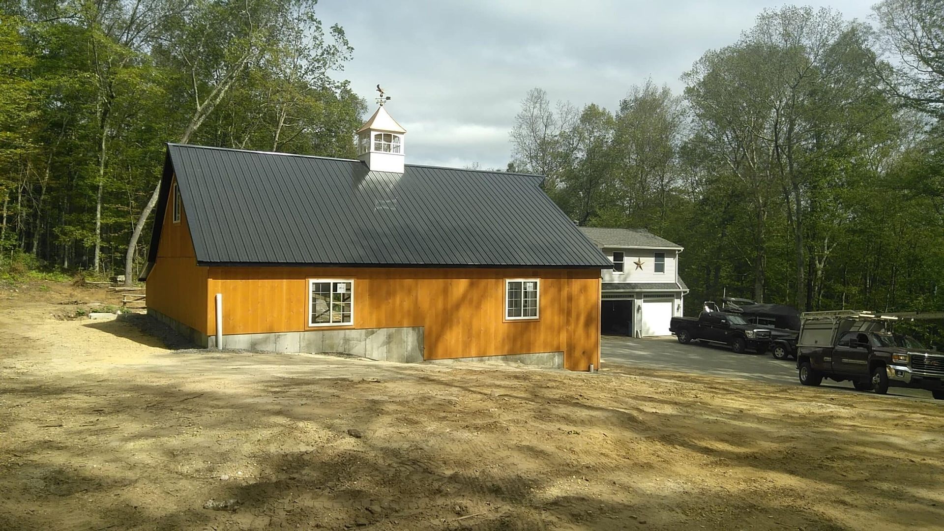 Orange wooden building with black roof beside dirt lot and parked cars, surrounded by trees