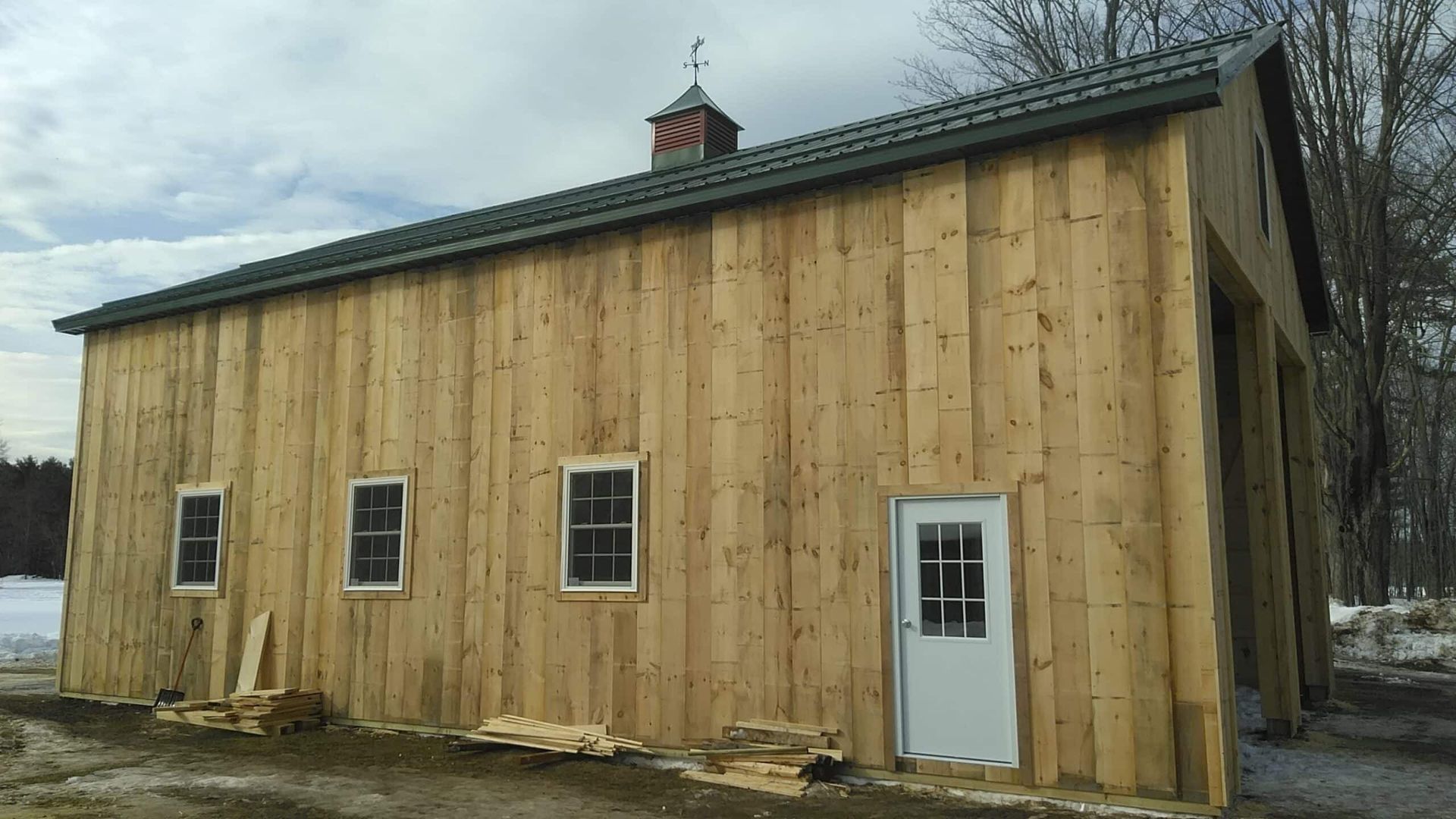 Wood-sided barn-like building with small windows and a white door on a snowy lot