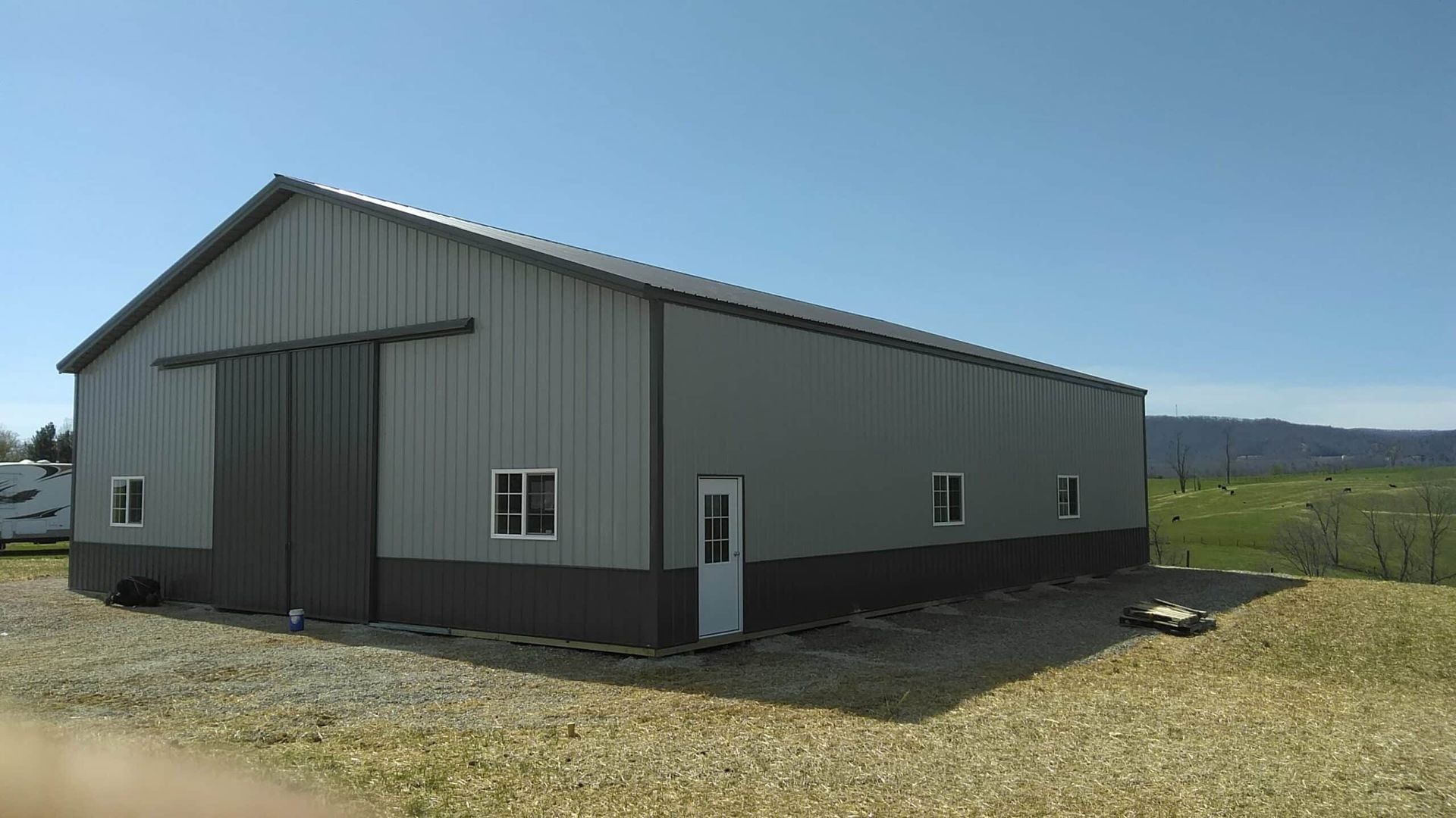 Gray metal barn-like building in a grassy rural field under a clear blue sky